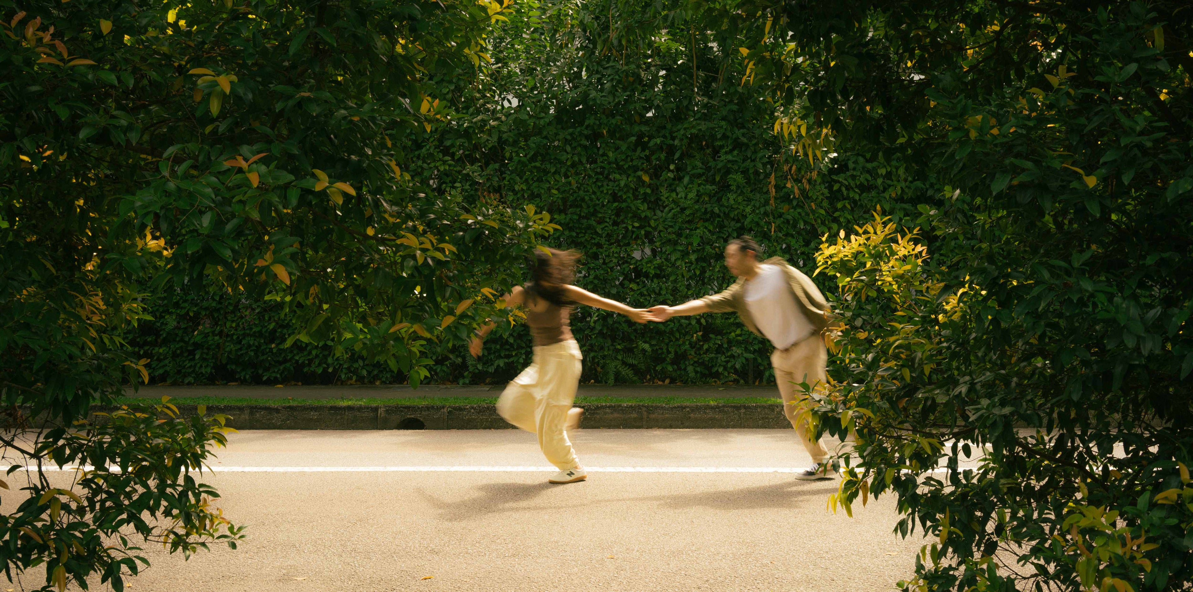 Two people holding hands on a road surrounded by greenery