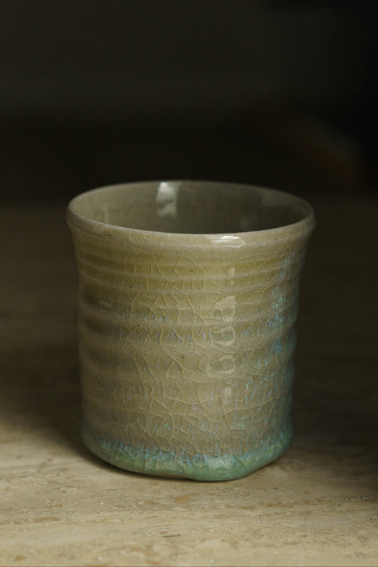 Sandy colored cup with small swirly ridges. Tinged faintly with blue and green throughout with more on the bottom.