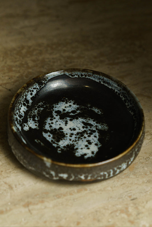 Small catchall dish in black with white patches.