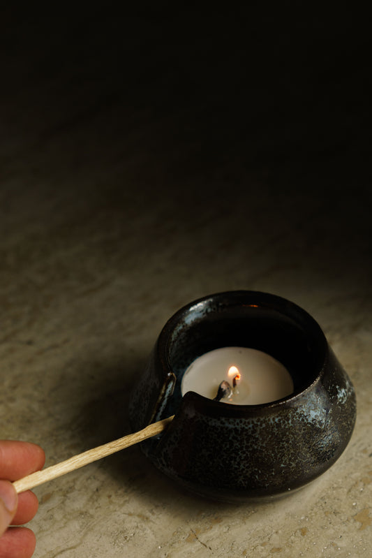 Angular candle holder in black with white patches. Has a small strip cut out of the wall with a match through it.