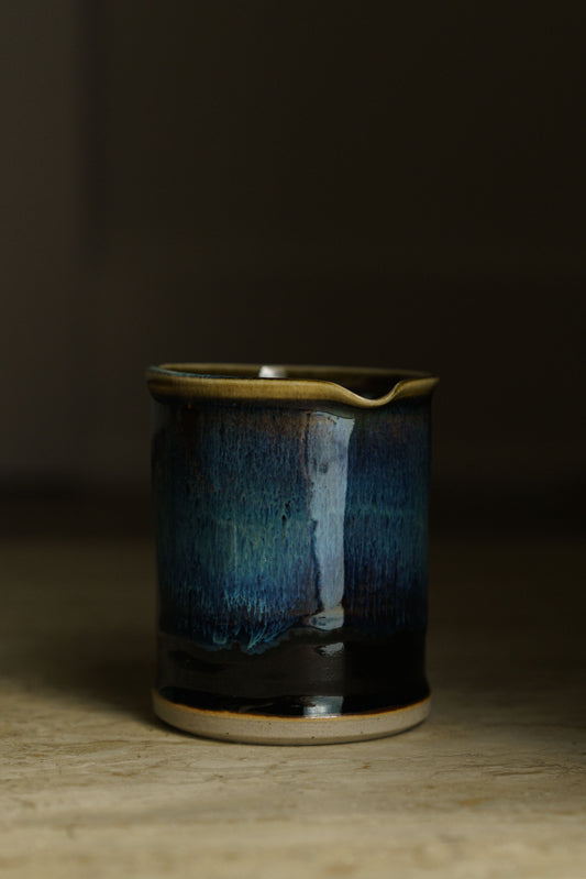 Black beaker with spout with white, blue, gold coloration  on the inside and and 75% of the outer wall.