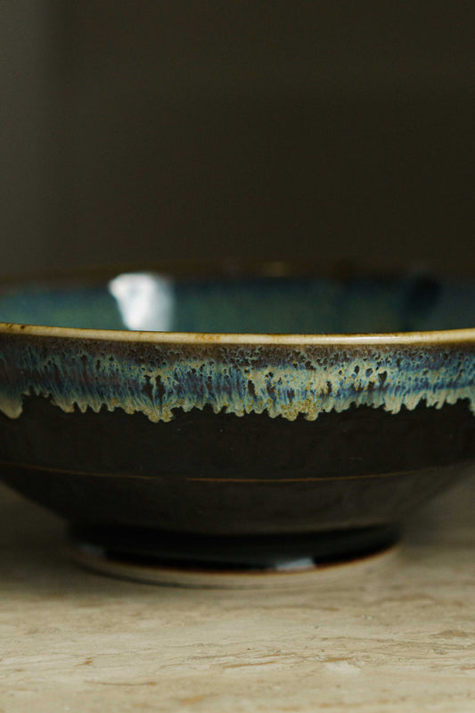 Black angular bowl with white, blue, gold coloration  on the inside and near the rim.