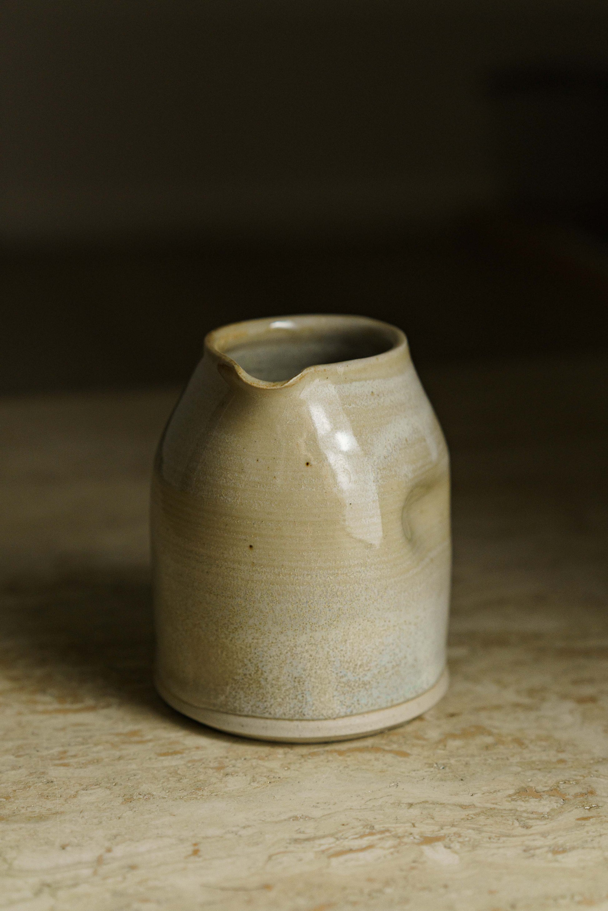 Cream colored spouted pourer with finger indent on the side.