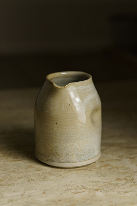 Cream colored spouted pourer with finger indent on the side.