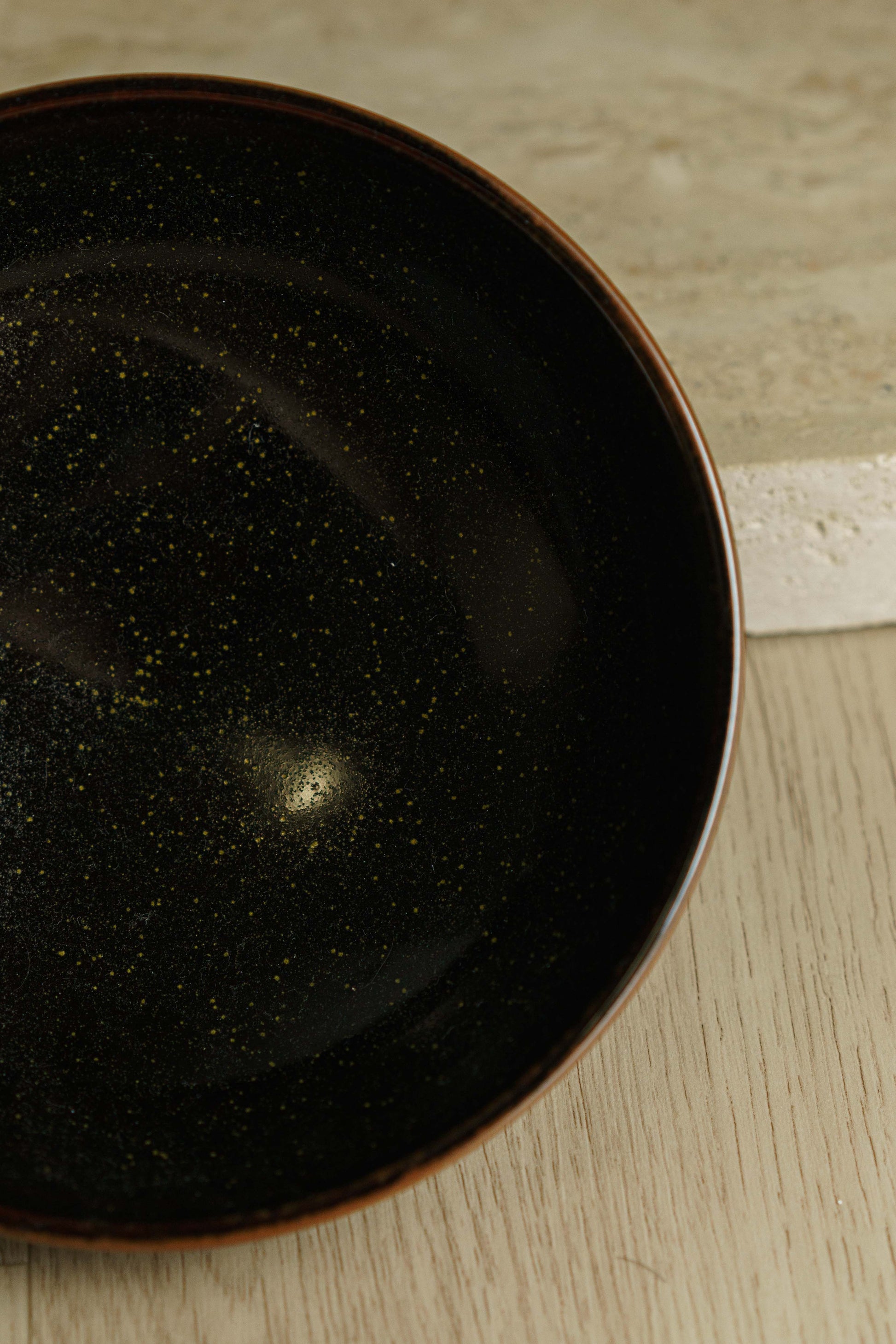 Black bowl with green flecks and angular outer wall.
