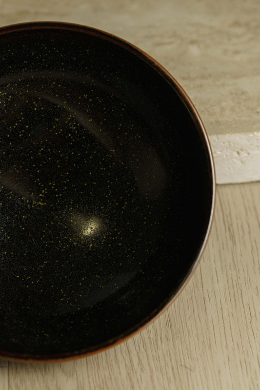 Black bowl with green flecks and angular outer wall.