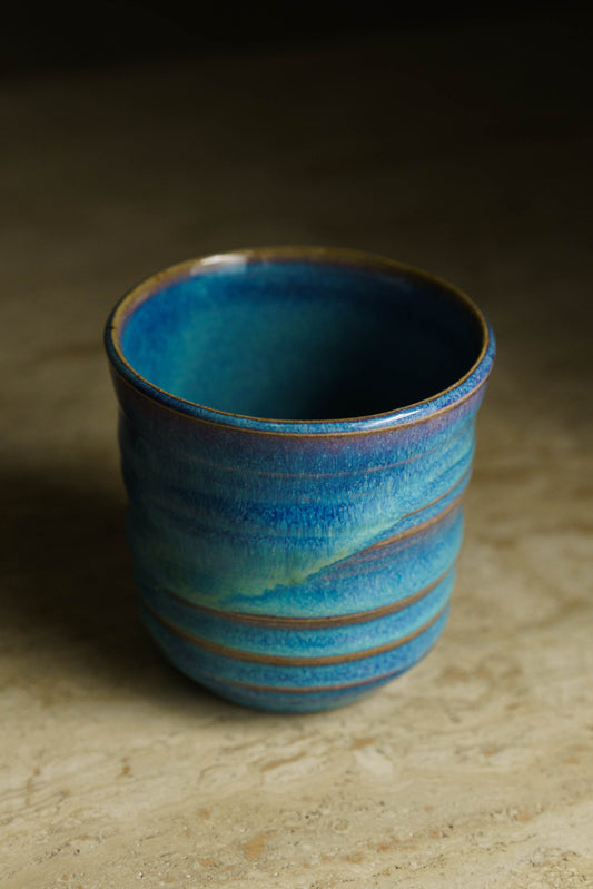Cup with several ridges on the outer wall. Glazed in a flowy blue and white.