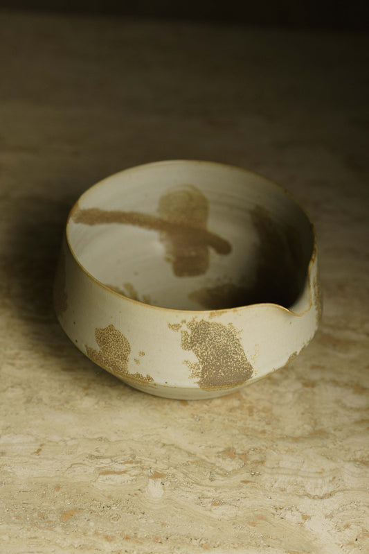 Spouted angular matcha bowl in white with brown spots.