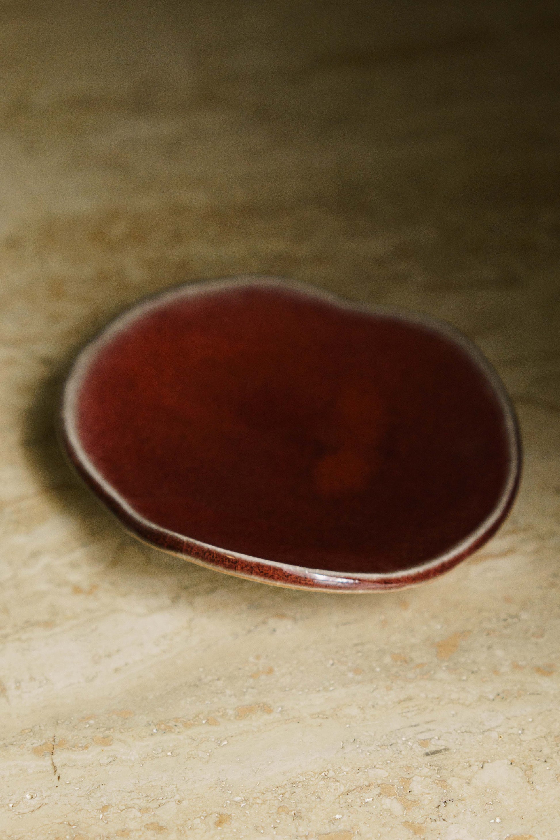 Small ceramic dish with a glossy red-brown glaze on a beige surface